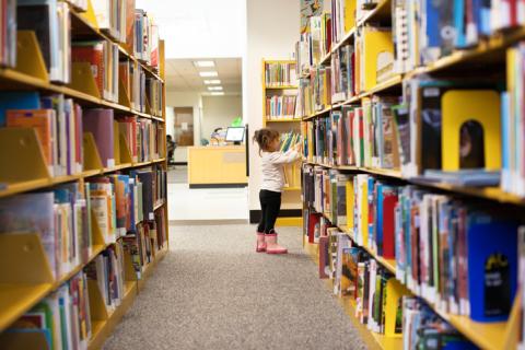 Young girl looking at library books on shelves.