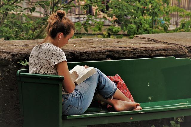 Woman reading on a park bench, with headphones in her ears