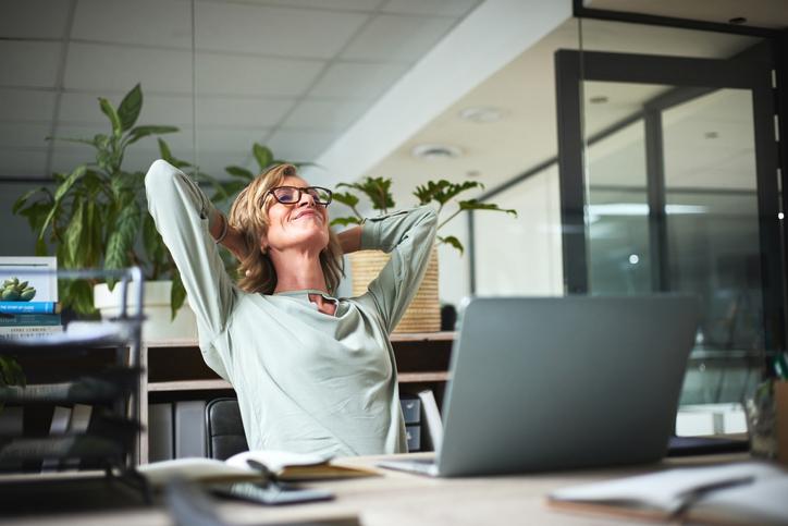 Smiling woman stretching at office desk with computer.