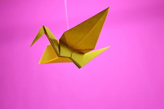 Yellow origami crane on pink background.